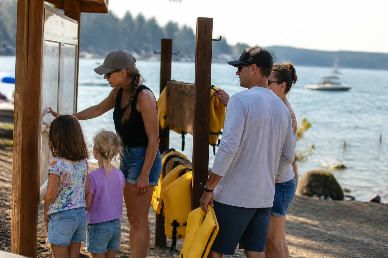 Families read the Honeysuckle Beach kiosk next to a life-jacket loaner station on Hayden Lake.