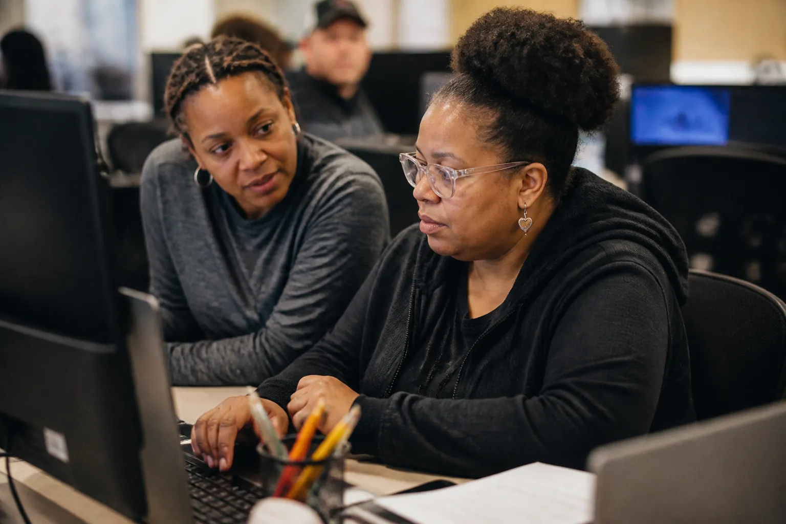 Member practices office skills at a computer with a staff mentor beside them in the clubhouse.