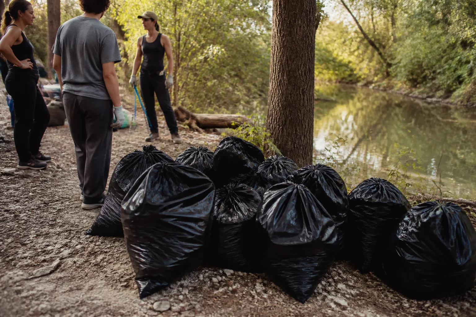 Black trash bags line the bank beside East Bouldin Creek as Make Austin Clean volunteers finish an Austin creek cleanup.