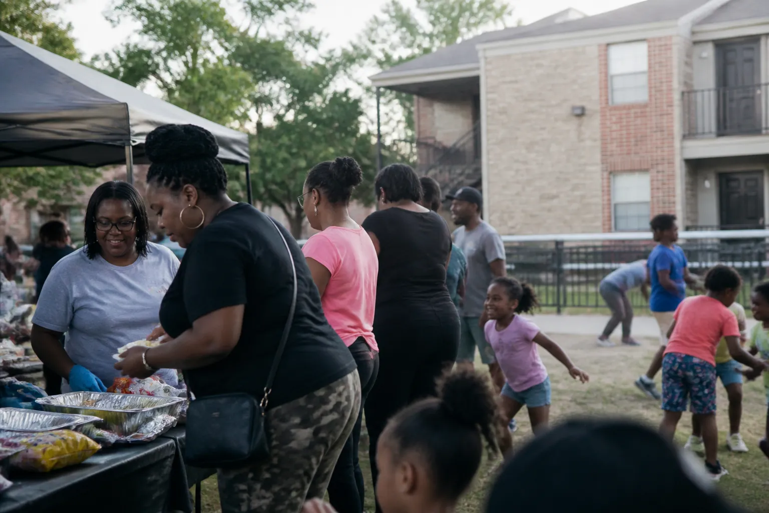 Families and Dallas City Homes staff gather outside apartments in Southern Dallas at a neighborhood event with food tables, showing where to donate for housing assistance in Dallas.