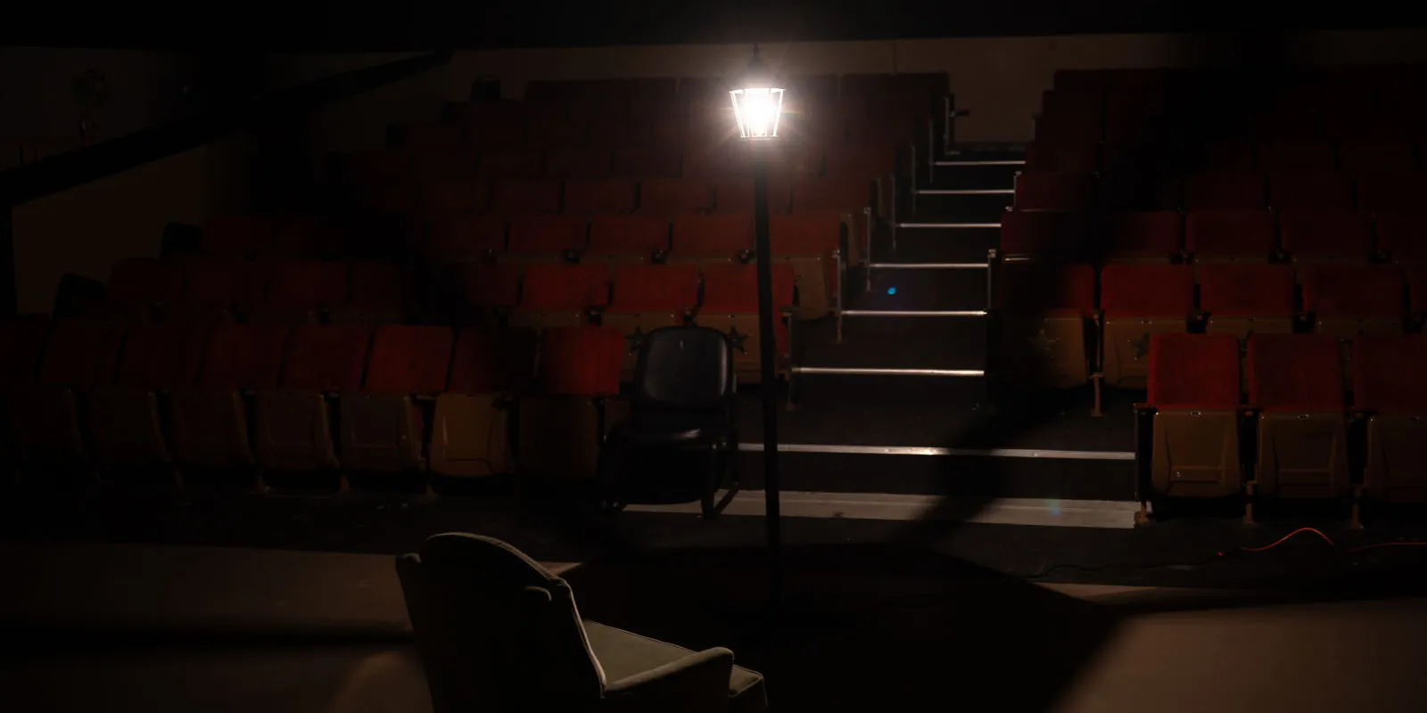 An empty theater with a single ghost light lit on stage.