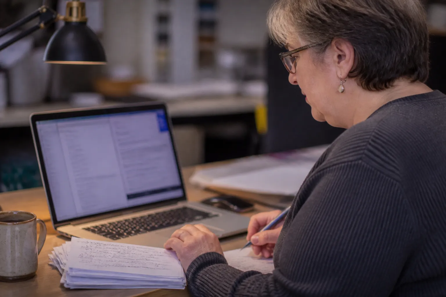 Volunteer judge reviews ThinkWRITE submissions on a laptop with handwritten feedback notes for teens.