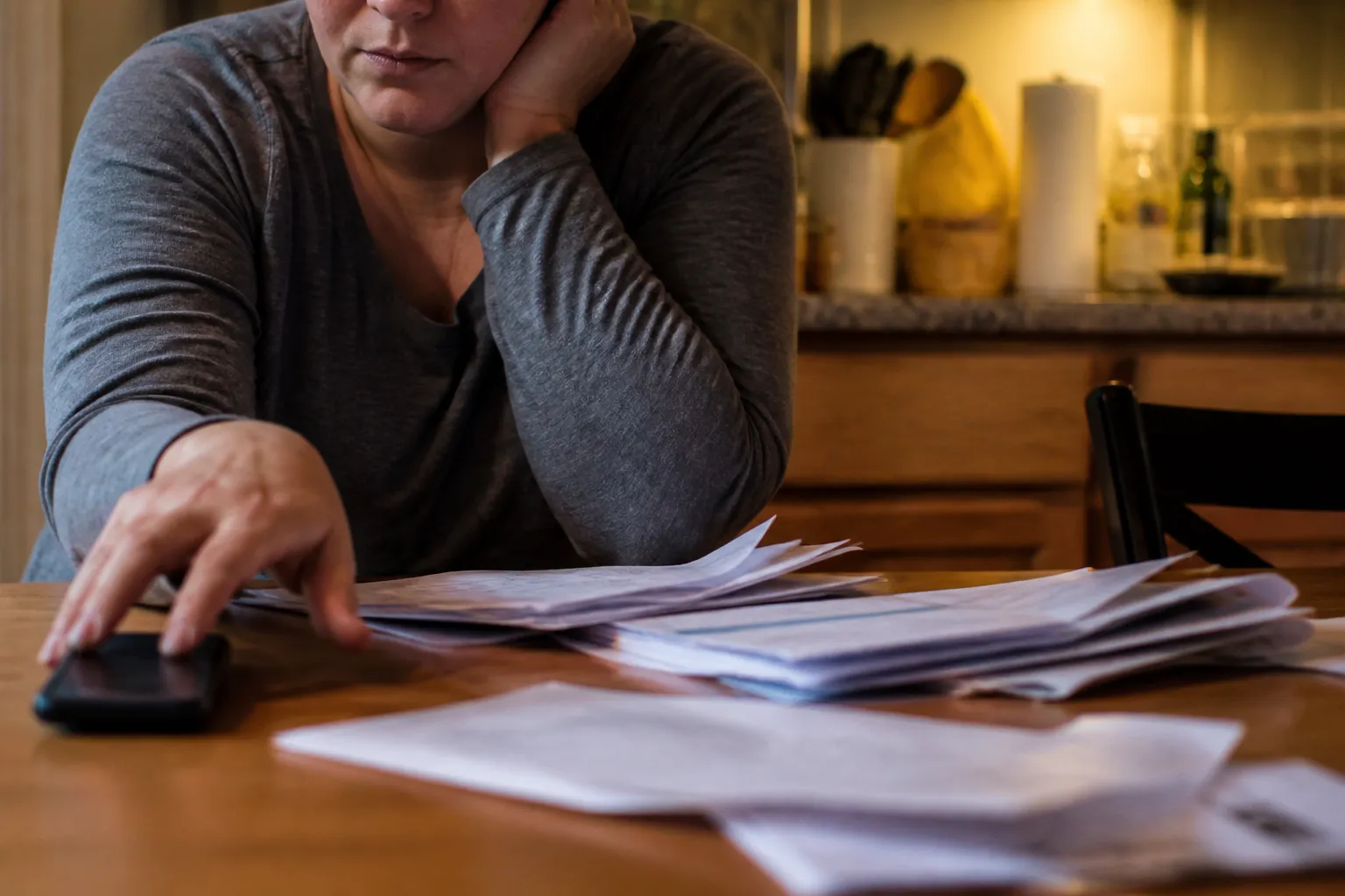 In Lincoln, a kitchen table shows bills and 24/7 helpline info next to a phone on the verge of a call.