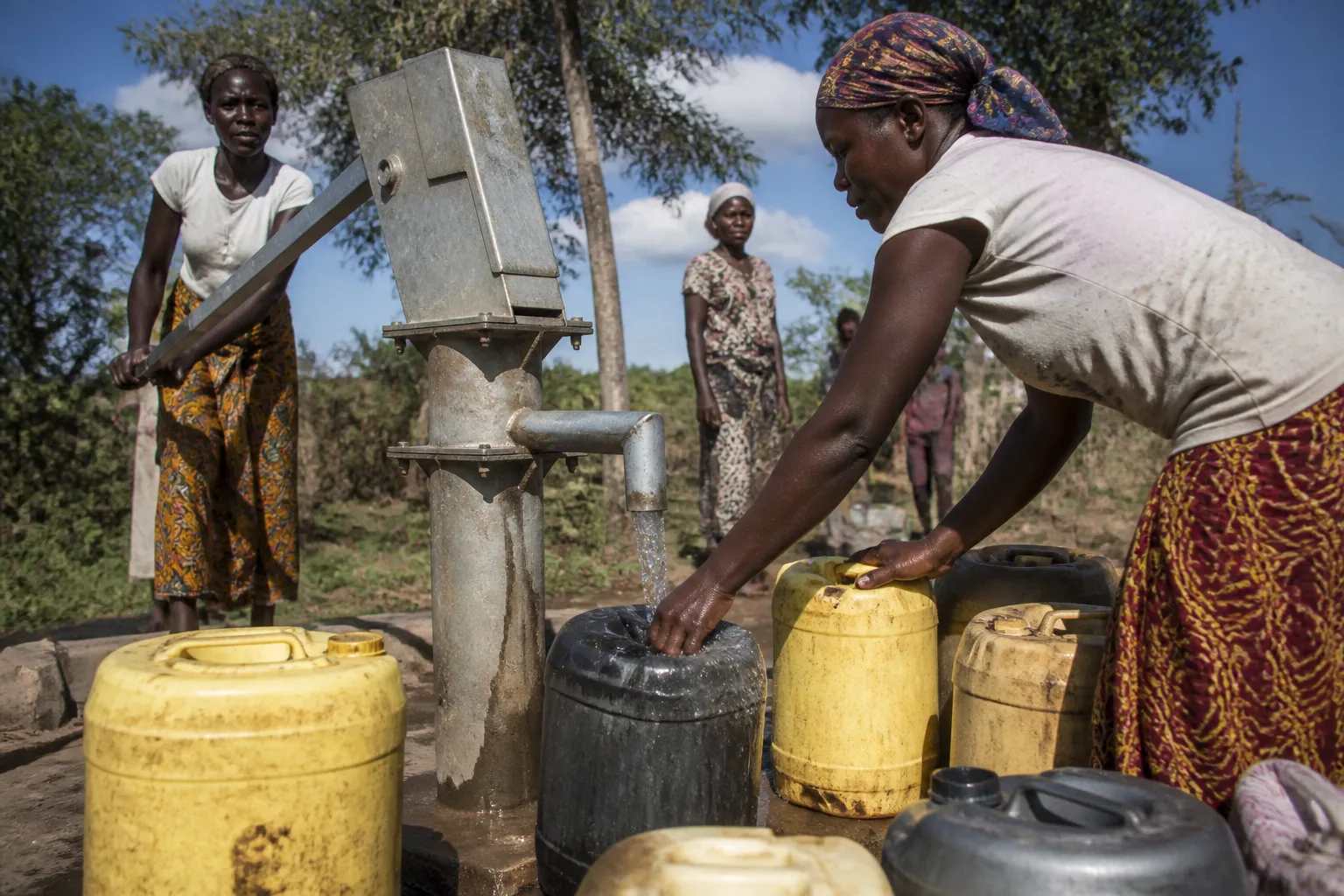 Families gather around a hand pump and water containers at Kenya KEEP’s Kamresi well in daylight.