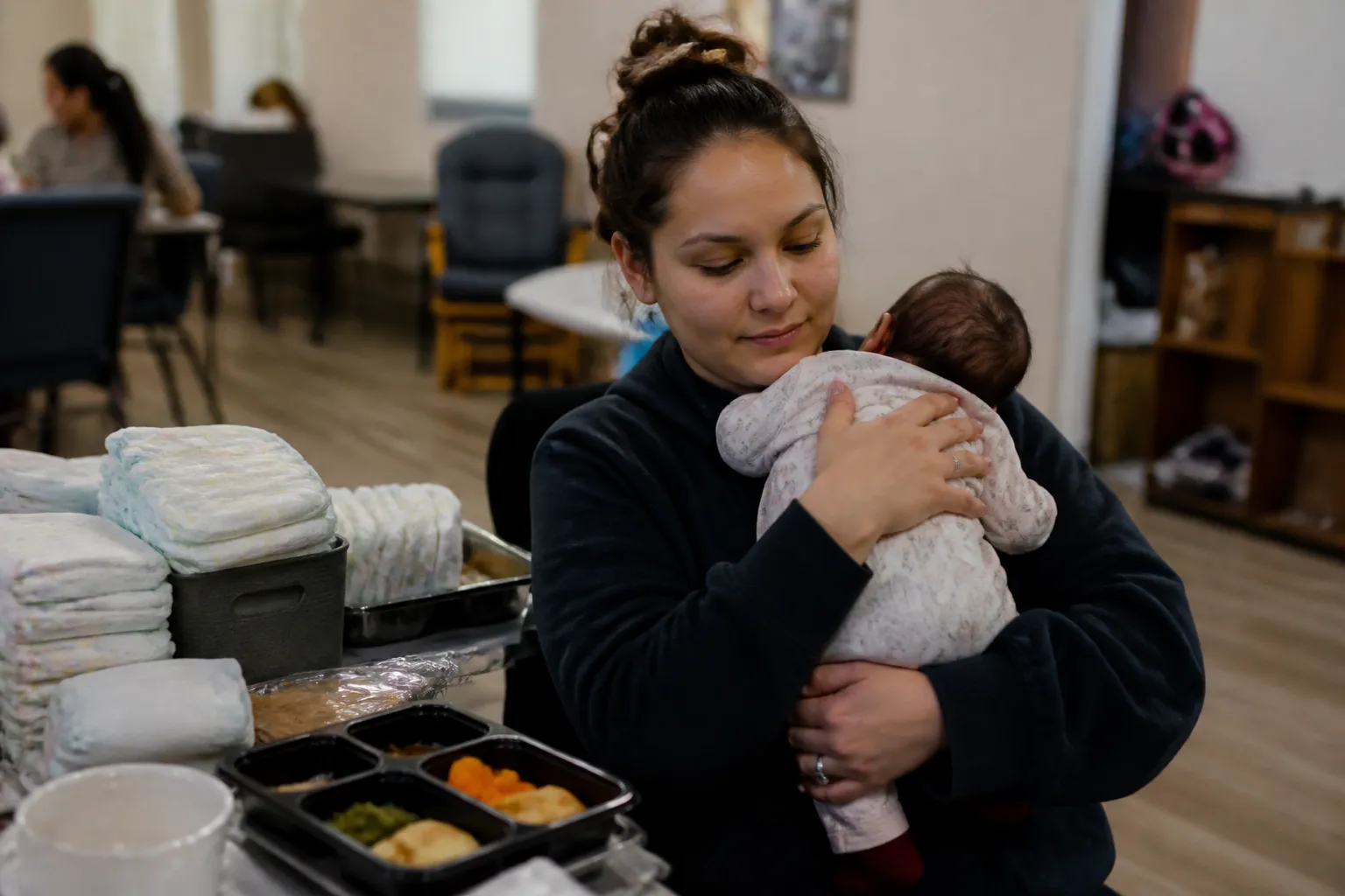 At Vita Nova Papillion, a young mother holds her baby after a life-skills class near diapers and supplies.