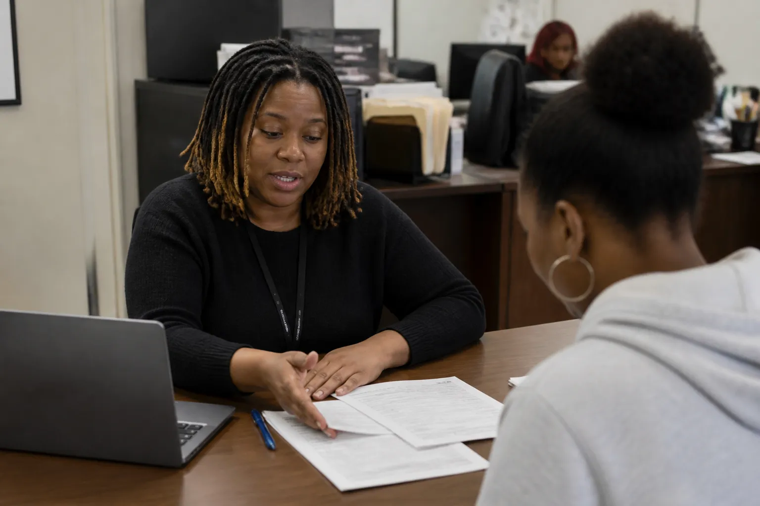 DEAC staff points a tenant to application links and printed court forms at an intake desk in Dallas.