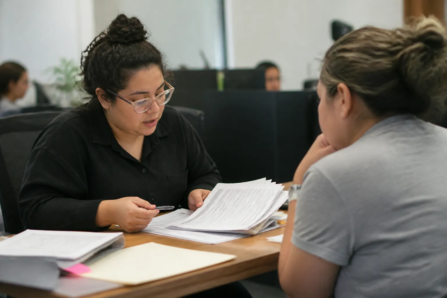 Inside Centro Aztlan, a staff member helps support immigrant families in Houston with tax documents and a USCIS checklist at a bilingual counter.