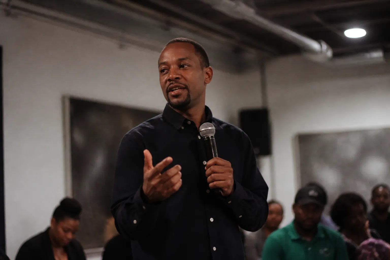 Chas Moore speaks at a community gathering in Austin with Austin Justice Coalition signage behind him.