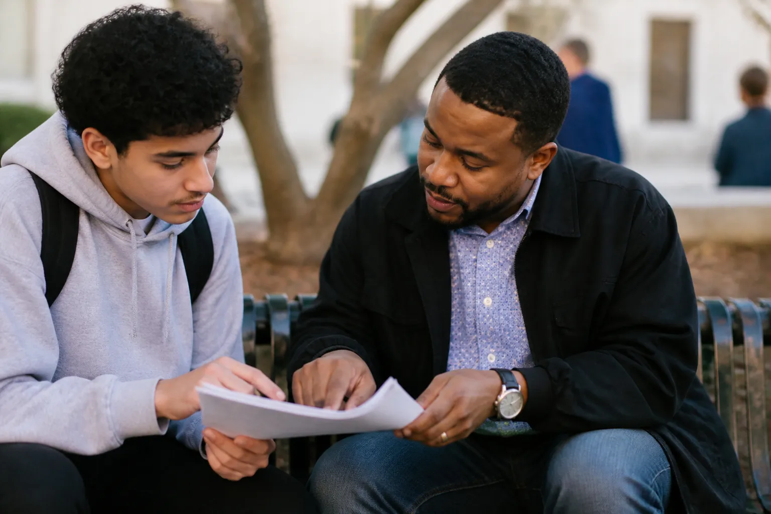 A Friend mentor and a high-school student review graduation plans on a campus bench after class.