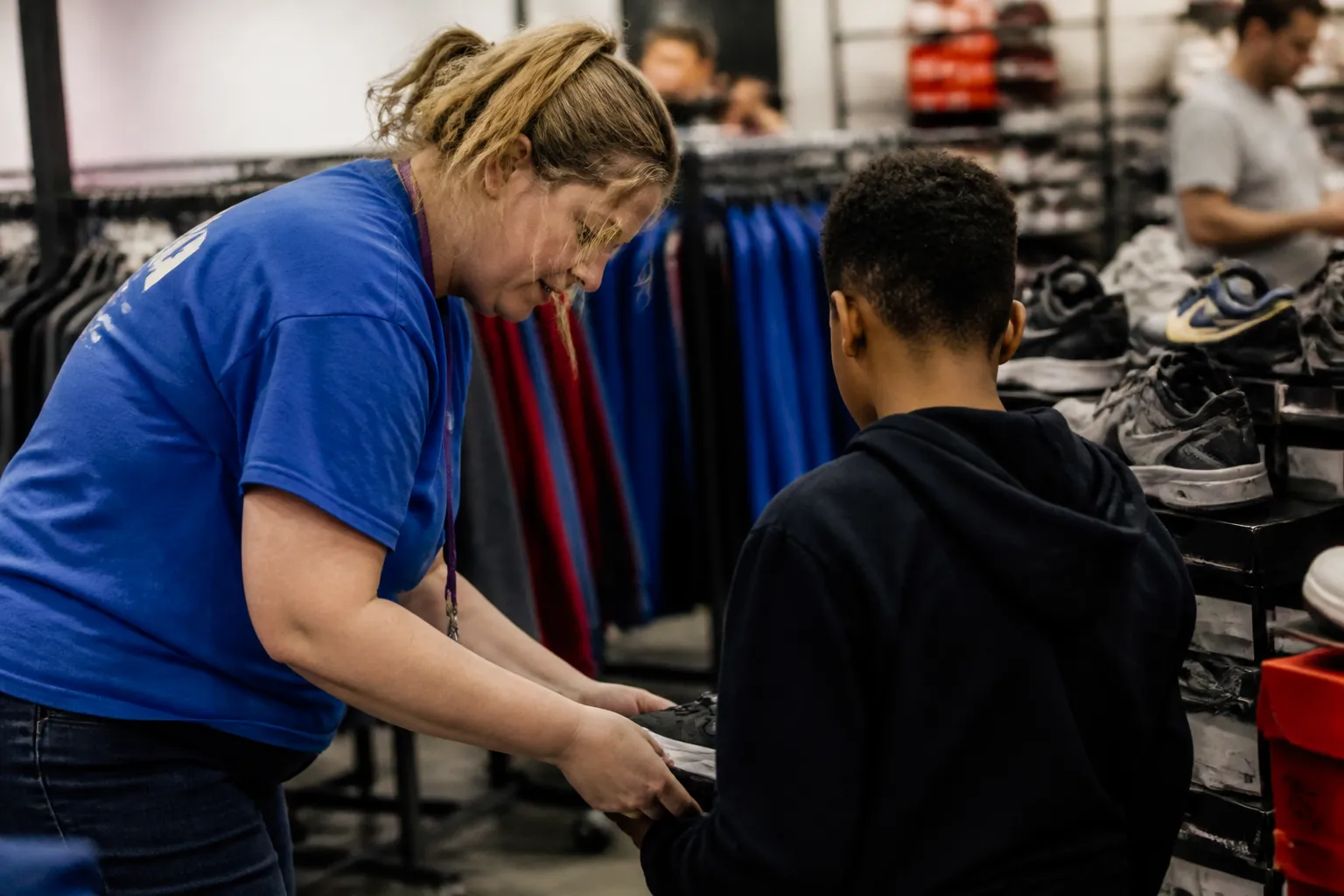 A Foster Heart & Hope volunteer assists a child with shoes and a hoodie at Trey’s Boutique in Ralston, a scene from the best youth charities in Omaha.