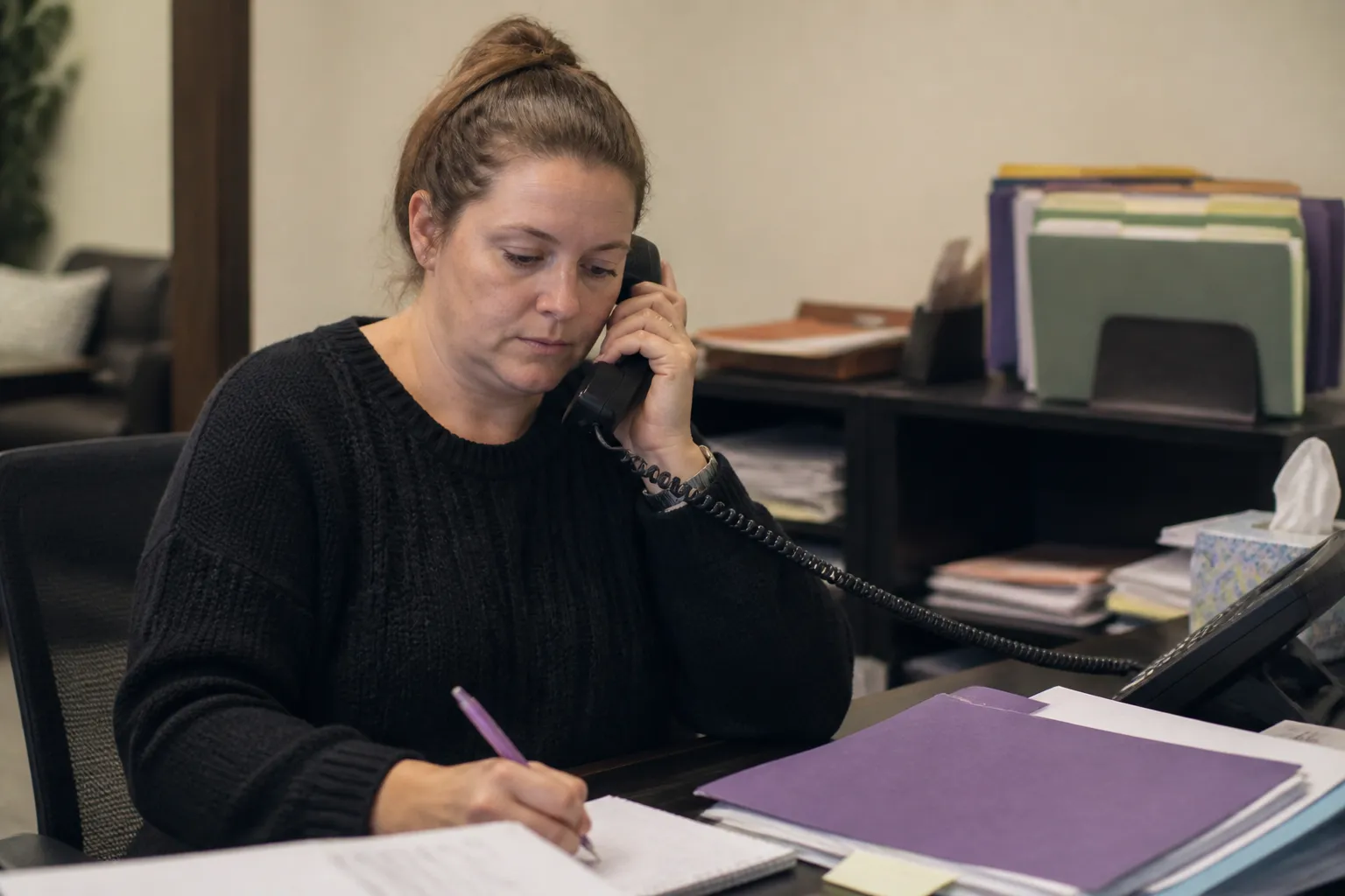A Voices of Hope advocate takes a crisis line call in Lincoln with resource folders and a notepad on the desk.