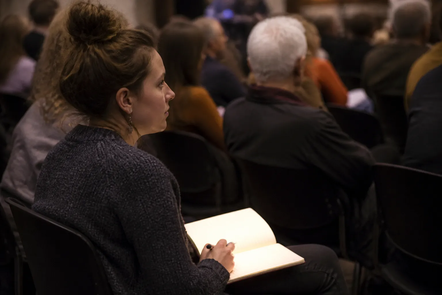 UM student in a sponsored seat with notebook open as audience Q&A begins at City Club Missoula.