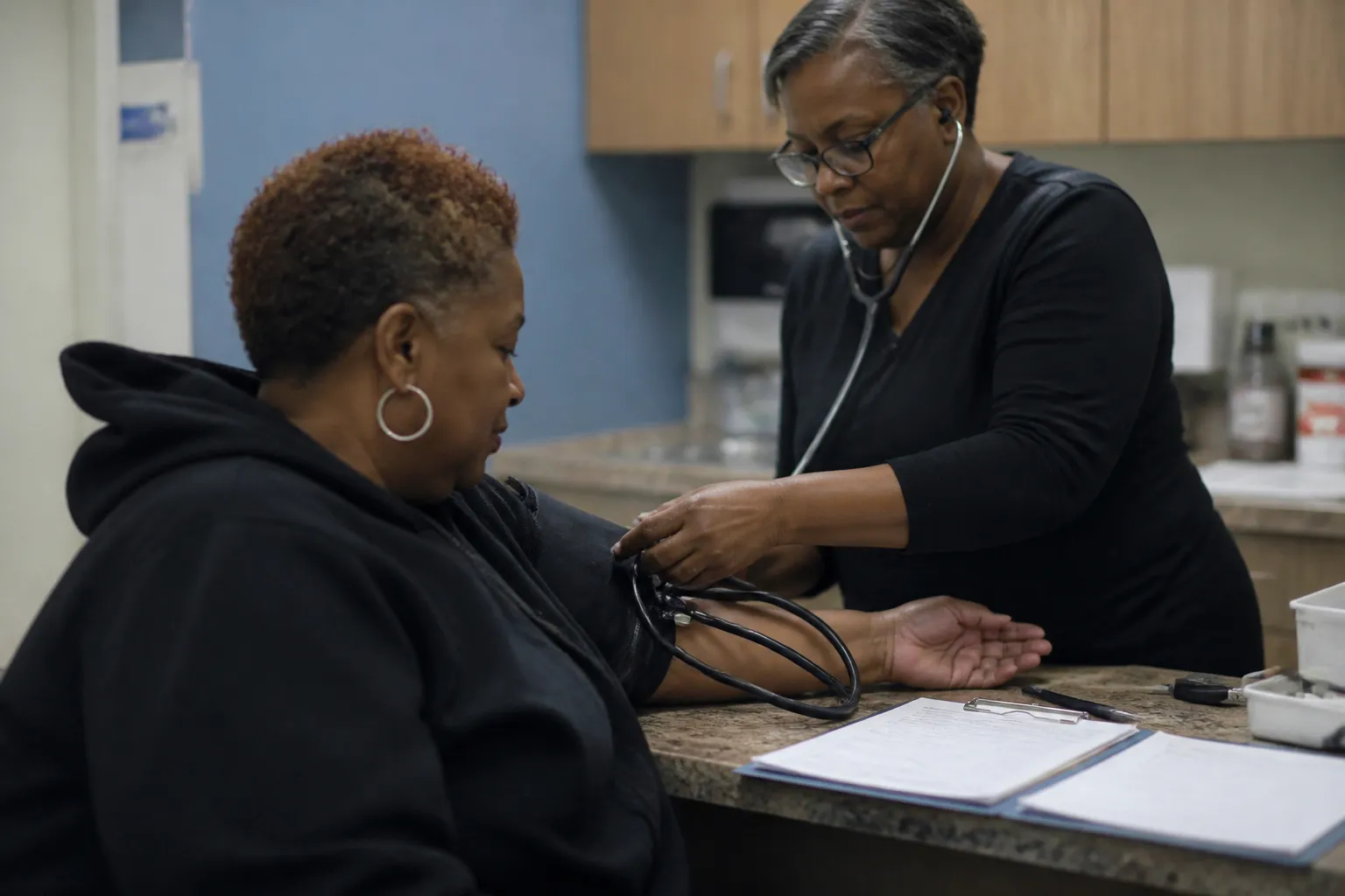 Clinician checks a patient’s blood pressure in a North Omaha exam room with intake forms on a counter.
